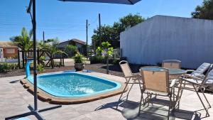a pool with chairs and a table and an umbrella at Casa com piscina aquecida, 3 quartos e 3 camas extras in Capão da Canoa