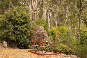 a table and two chairs sitting in a forest at Wattle Grove Hideaway by Tiny Away in Wattle Grove