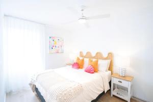a white bedroom with a bed with pink and orange pillows at The Chelsea Beachside Apartment in The Entrance