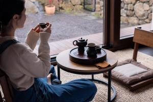 a woman sitting on the floor drinking a cup of coffee at 바티하우스 in Ara-ri