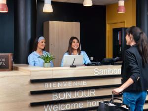three women are sitting at a reception desk at Aparthotel Adagio Access Paris Asnières in Asnières-sur-Seine