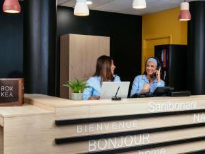 two women sitting at a desk talking on a cell phone at Aparthotel Adagio Access Paris Asnières in Asnières-sur-Seine