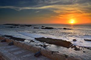 um pôr-do-sol sobre o oceano com pedras na água em La Maison des Artistes em Essaouira