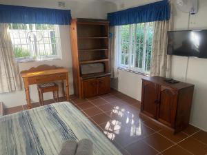 a room with a bed and a television and a desk at Fishermans Cottage - BillsBest in Port Edward