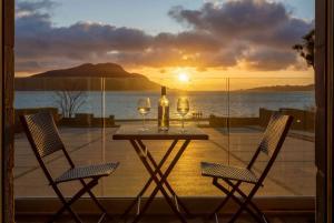 a table with two wine glasses on a balcony with the sunset at Arran Shores Luxury Shorefront Suite 1 in Lamlash