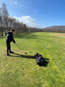 a man is holding a golf club and pulling a bag at Shetland Cottage Kincraig in Kincraig
