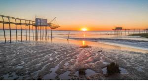 a sunset on a beach with a pier and the ocean at Studio cocooning entre Fouras et Rochefort in Saint-Laurent-de-la-Prée