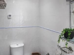 a white tiled bathroom with a toilet and a plant at The Lookout in Pendine +4 photos