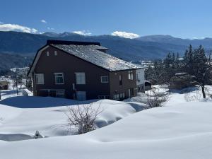 a house covered in snow with mountains in the background at Togari Sunshine Lodge in Iiyama