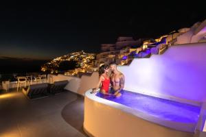 a couple sitting on the edge of a swimming pool at night at Pegasus Suites & Spa in Imerovigli