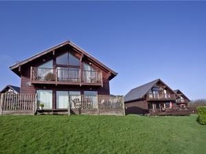 a large wooden house with a balcony on a green field at Ash Lodge - Retallack in Saint Columb Major