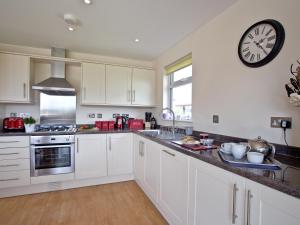 a kitchen with white cabinets and a clock on the wall at Cedar Lodge - Retallack in Saint Columb Major