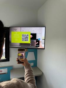 a person taking a picture of a tv with a cell phone at First Inn Hotel Blois in Blois
