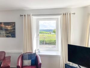 a living room with a window and a chair and a television at Dalvista Cottage in Leurbost