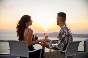 a man and a woman sitting at a table with a drink at Pegasus Suites & Spa in Imerovigli