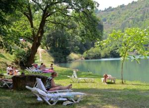 a group of people sitting in the grass near a lake at ZEcamping 4 étoiles familial animaux acceptés animé équitation in Saint-Rome-de-Tarn