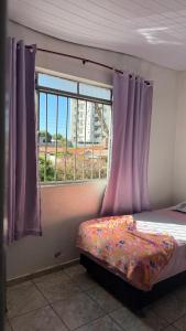 a bedroom with a bed with purple curtains and a window at Pousada da Salete in Campo Mourão