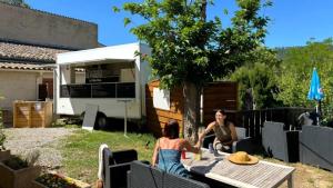 two women sitting at a table in a backyard with a caravan at ZEcamping 3 étoiles animations à 2 km du lac de Sainte Croix in Moustiers-Sainte-Marie