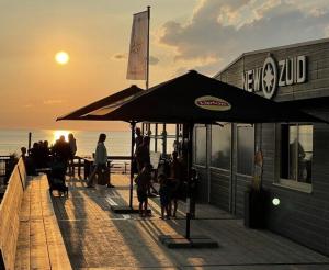a group of people standing on a pier with an umbrella at Zee aan Geluk in Sint Maartensvlotbrug