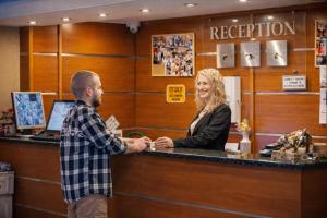 Ein Mann und eine Frau schütteln sich an einem Empfangstresen die Hände. in der Unterkunft Hotel Elit in Dewin