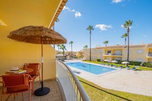 a balcony with a table and an umbrella and a swimming pool at Jardins Vale de Parra in Albufeira