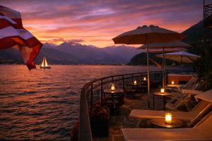 a restaurant with tables and umbrellas and a sailboat in the water at Hotel Meridiana in Bellano
