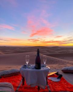 a table with a bottle and two glasses on the desert at Royal Erg Chebbi Luxury Camp in Adrouine