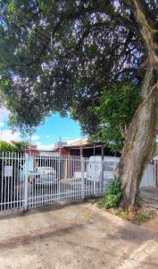 a white fence with a tree in front of it at Pousada Recanto Alaketu Hospedagens in Campo Grande