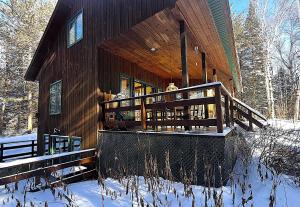 a wooden house with a deck in the snow at Le Domek de nature apaisante in Sainte Béatrix