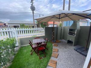 a patio with a table and chairs and an umbrella at Conforto na praia 2 Quartos com Ar Até 6 Pessoas in Imbituba