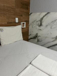 a bedroom with a white bed with a marble wall at Pousada Cantinho da Jú in Pirenópolis