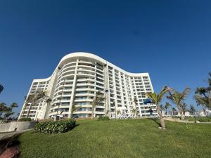 a large white building with palm trees in front of it at Departamento Playa Punta Diamante in Acapulco