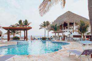 a pool at a resort with palm trees and the ocean at Dos Mundos Pacific Resort in Monterrico