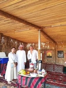 a group of three men standing next to a table at Endless Dunes Camp in Badīyah