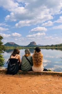 three people sitting on the shore of a lake at Elephant point tree house in Sigiriya