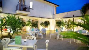 a patio with white tables and chairs and plants at Hotel Kaos in Villaggio Pirandello +5 photos