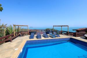 a swimming pool with chairs and the ocean in the background at Pousada Mirante dos Papagaios in Búzios