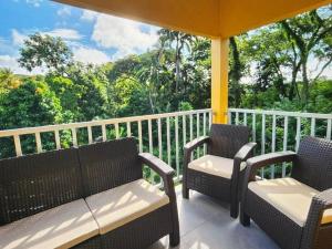 a porch with two chairs and a view of the forest at Tropical Tobago in Riseland