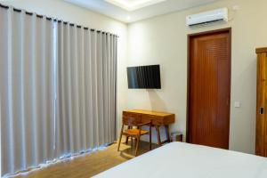 a bedroom with a bed and a desk and a television at Aditya House in Ubud