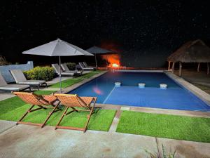 ein Swimmingpool bei Nacht mit zwei Stühlen und einem Sonnenschirm in der Unterkunft Brisa Bliss in San Juan de Alima