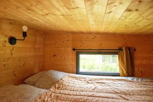 a bed in a wooden room with a window at Tiny house gite bucolique Brocéliande Hébergement insolite et centre bien être in Saint-Brieuc-de-Mauron