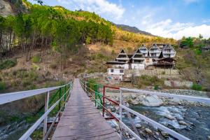 a bridge over a river with houses on a hill at Raj Villas by Jomotel - A Riverside Retreat in Banjār