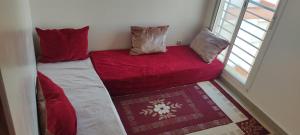 a small room with a bed with red sheets and pillows at Appartement à Sable d'or tanger in Tangier