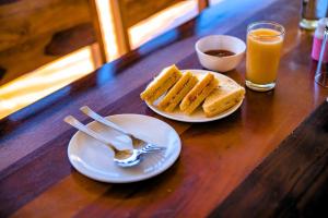 a table with two plates of bread and a glass of orange juice at Raj Villas by Jomotel - A Riverside Retreat in Banjār