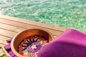 a wooden bowl filled with flowers on a table next to the water at Hurawalhi Island Resort in Kuredu