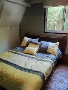 a bed with yellow and blue sheets and a window at Mini cabaña in Pucón