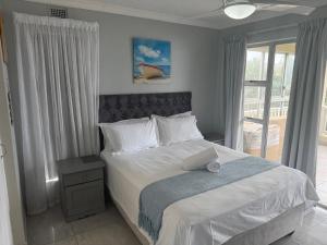 a bedroom with a bed with white sheets and a window at 64 Laguna La Crete in Uvongo Beach