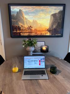 a laptop computer sitting on a wooden table with a painting at Private room in sharded apartment at Løren in Oslo