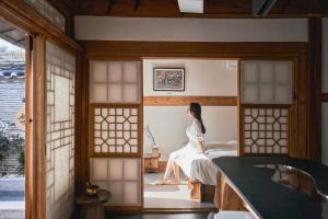 a woman sitting on a bed in a room at THE CHAE Premium Hanok Stay in Seoul