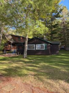 a log cabin with a tree in the yard at Northwoods Lake Content Cabin in Saint Germain
